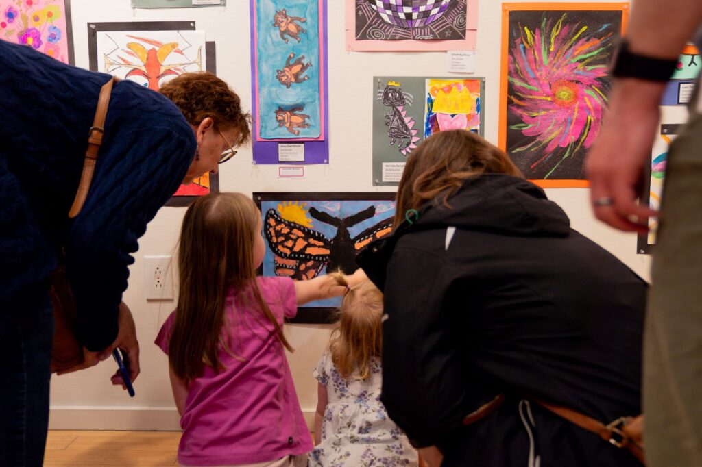 two adults and two young kids admire a butterfly painting