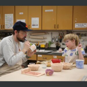 an adult and child painting glaze onto pottery