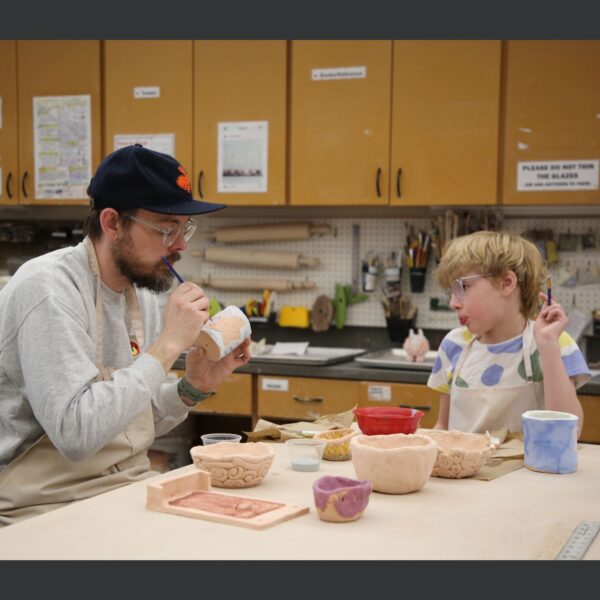 an adult and child painting glaze onto pottery