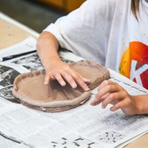 a preteen's hands working on a clay plate